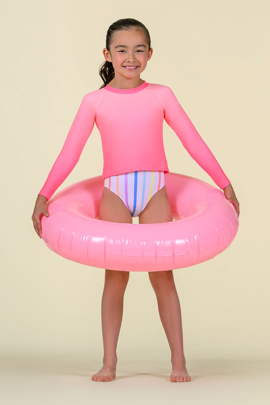 Child wearing a pink long-sleeve swim rash guard holding a pink inflatable ring