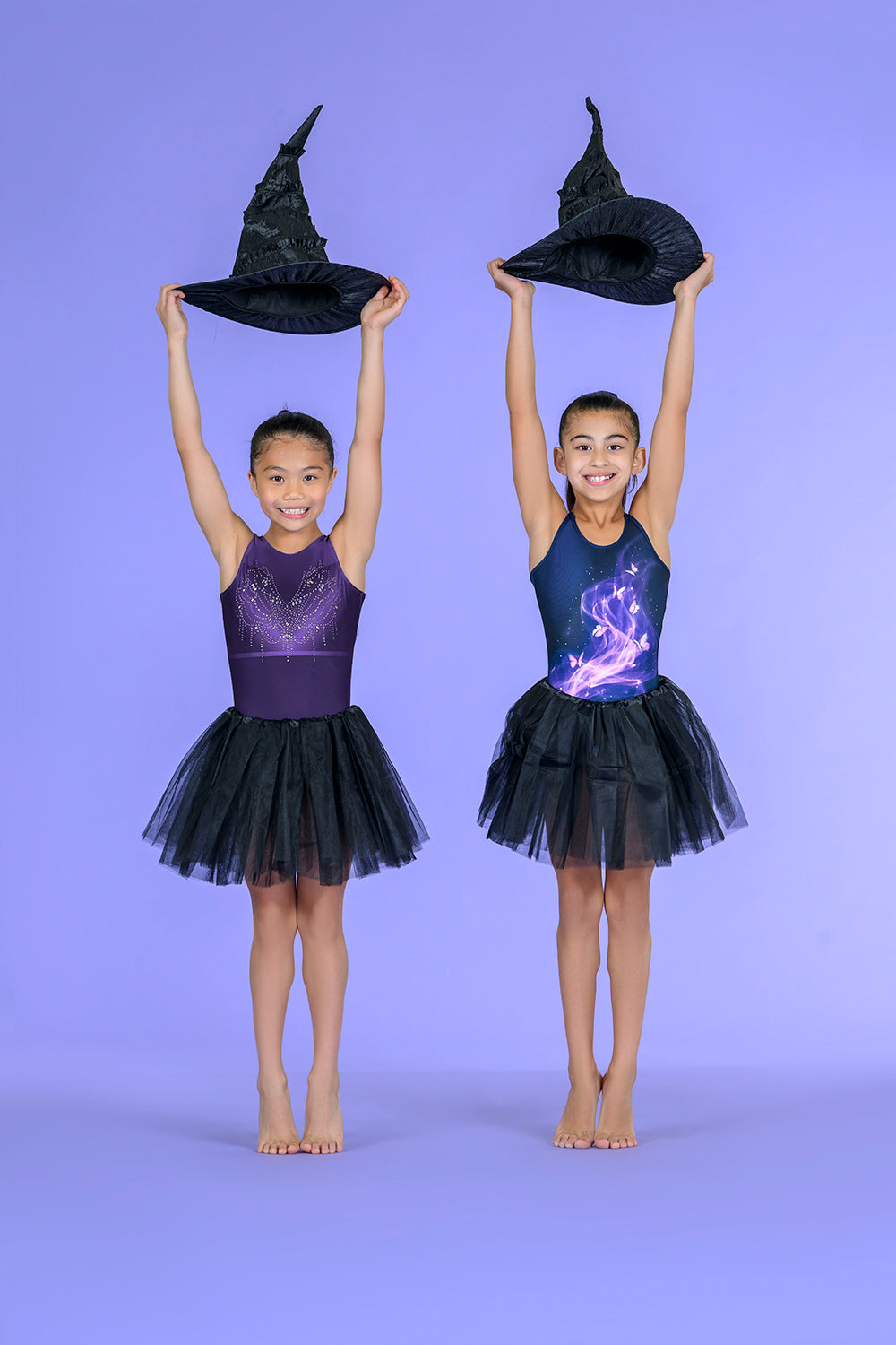 Two young girls in Destira leotards wearing black tutus, each holding a black witch hat above their heads. Halloween 2026