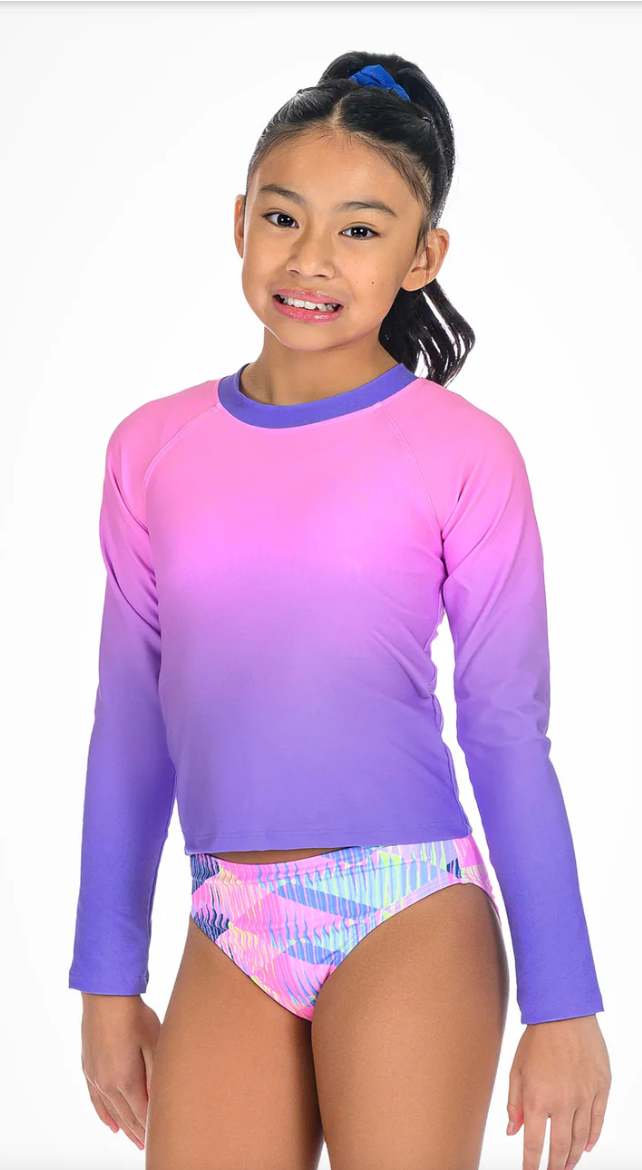 Young girl wearing a colorful long-sleeve rash guard and swim bottoms on a white background