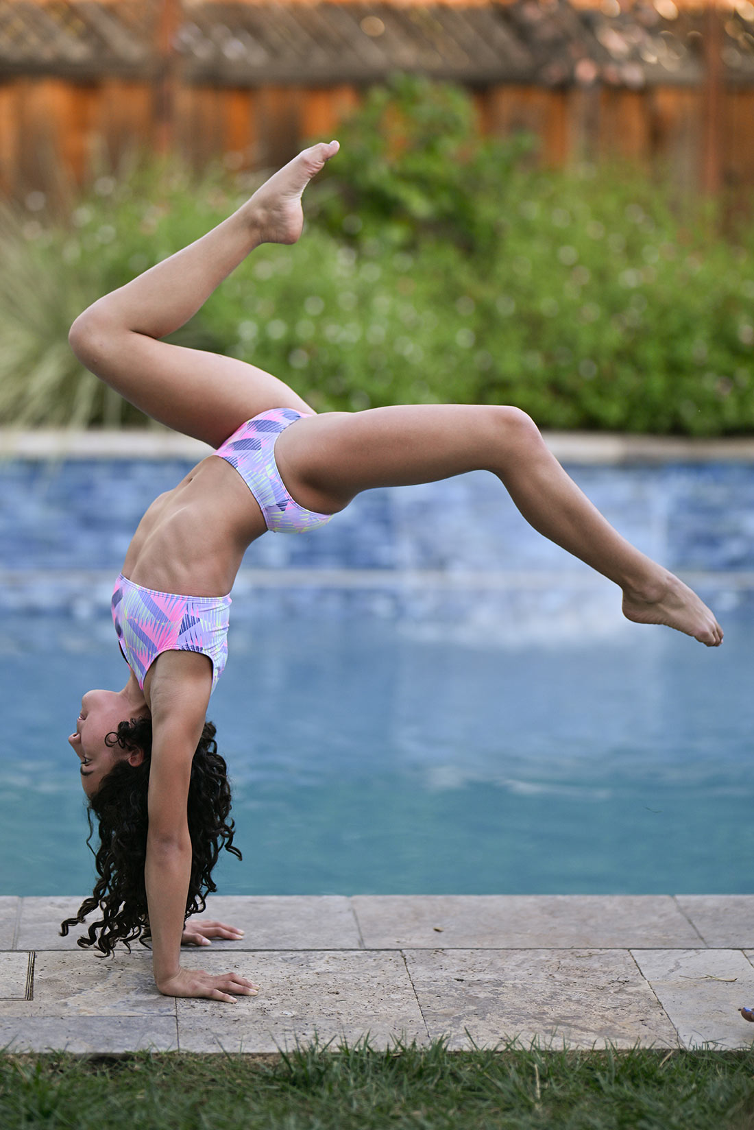 Gymnast doing a back walkover by a pool with a colorful pink and purple swimsuit