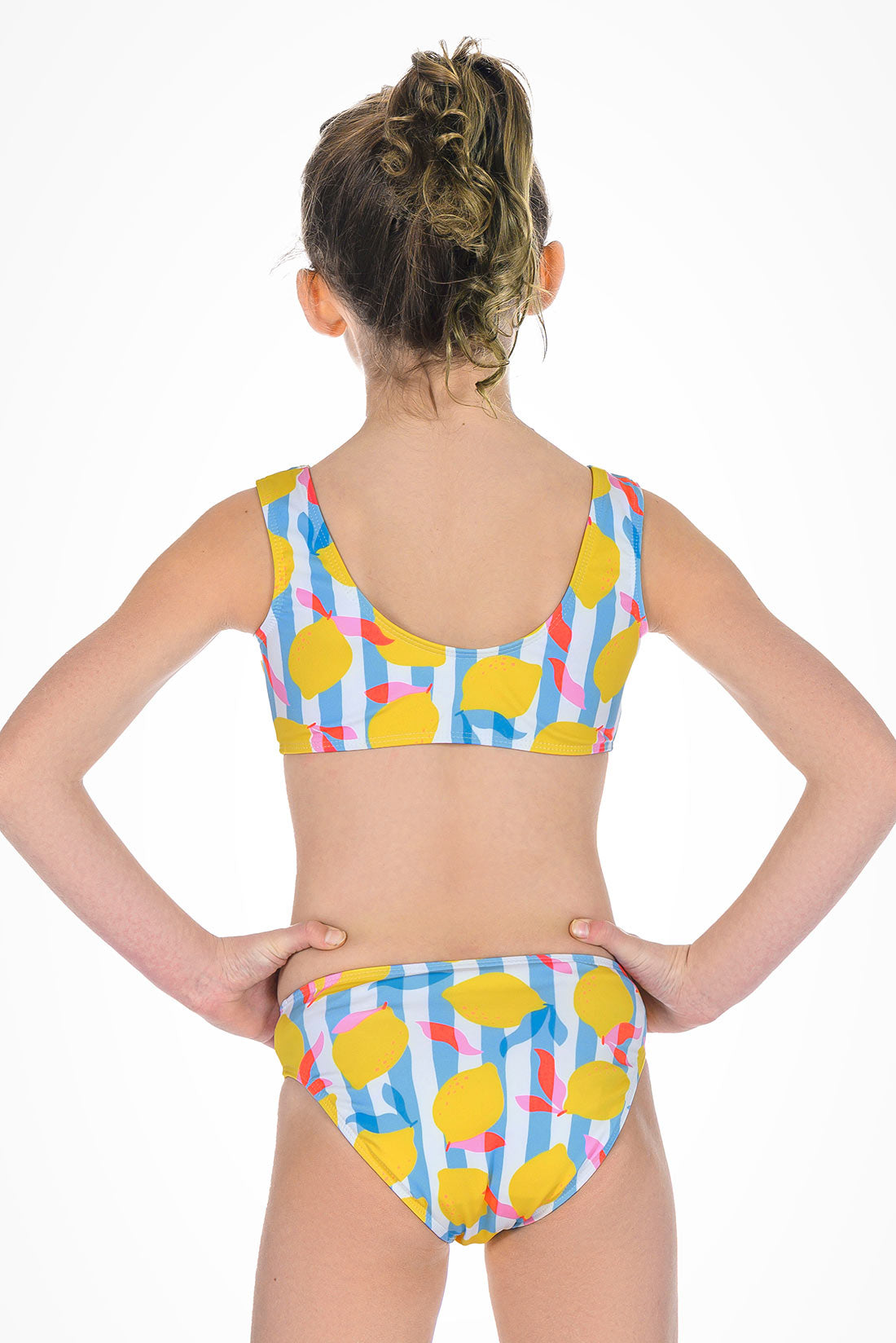 Child wearing a colorful bikini with lemon pattern on a white background showing back view