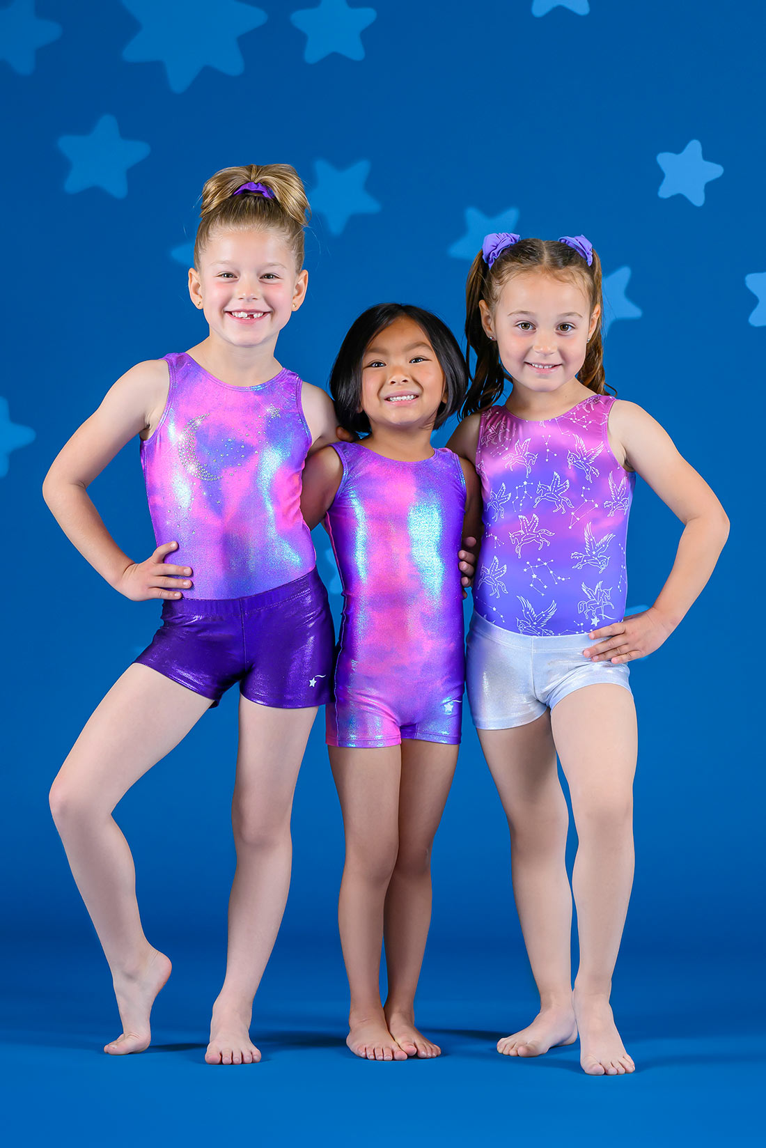 A trio of young gymnasts wearing pink and purple gymnastics leotards with shorts by Destira, 2023